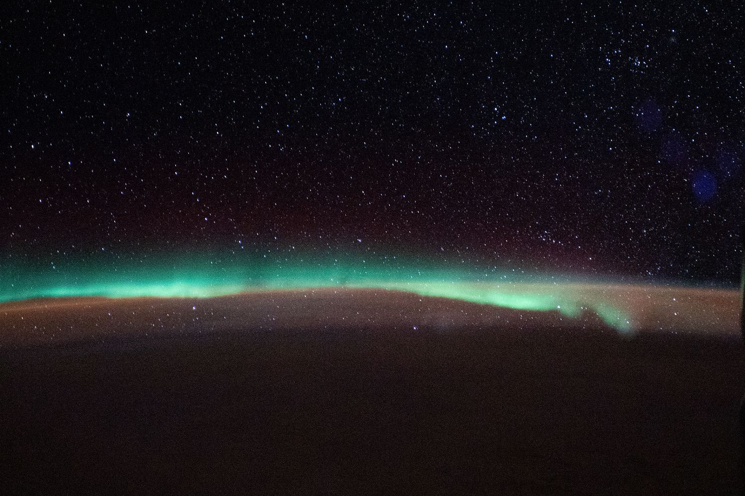 A band of green aurora along the curve of a planet's night side, stars above, seen from orbit.