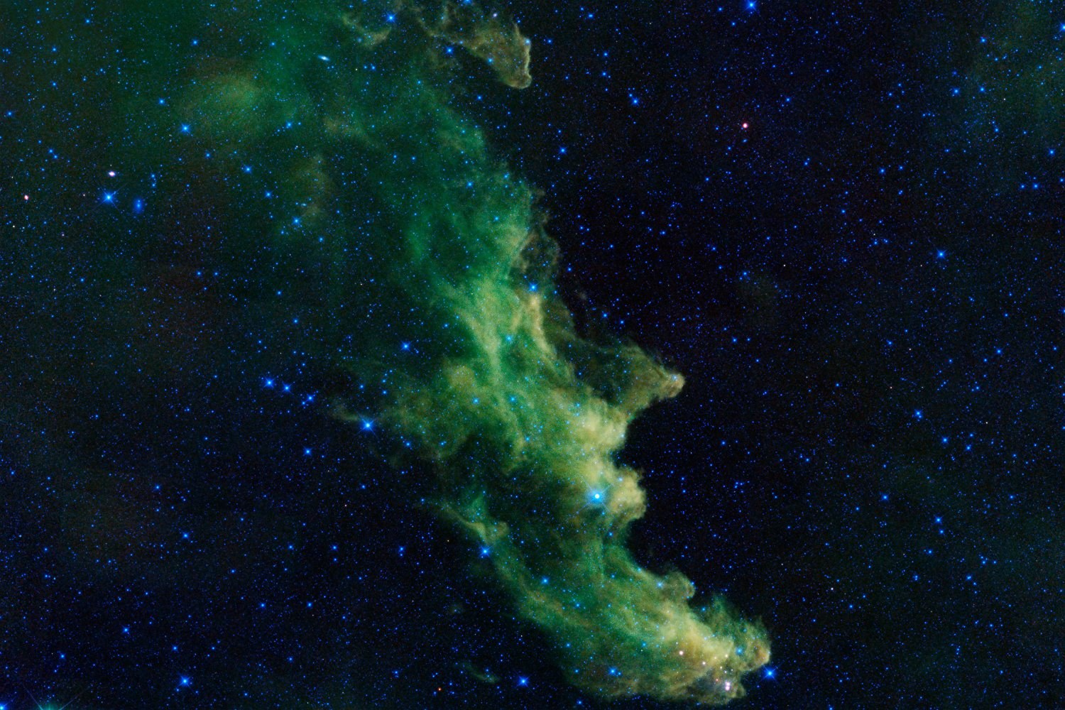 A green, witch-shaped cloud of gas among countless stars, in false colour.