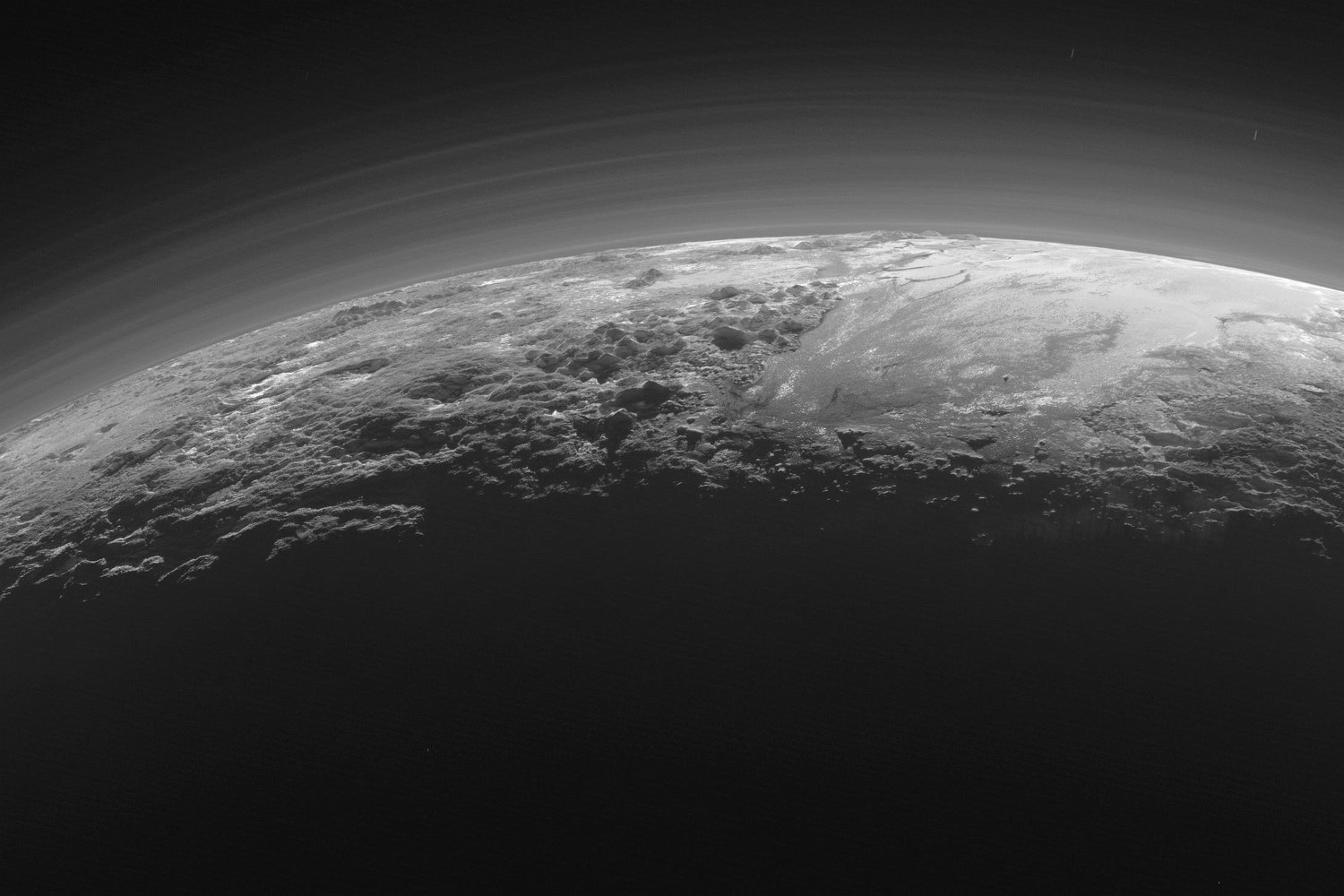 Icy mountains and smooth plains under layers of haze, lit by a low sun, in black and white.