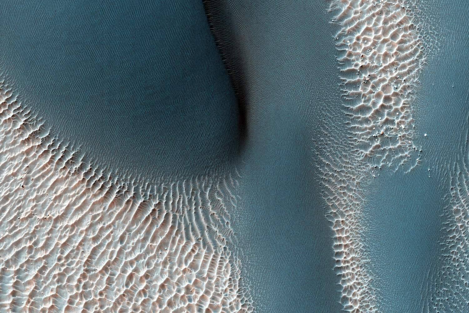 Blue-grey dunes with pale rippled sand between them, seen from above.