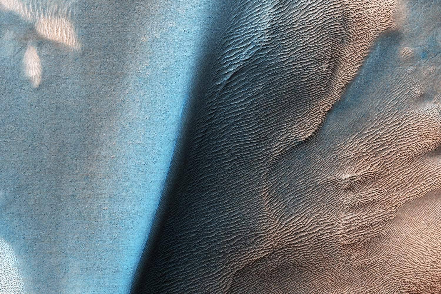 A long teal-blue dune flank beside pale, rippled ground, seen from above.
