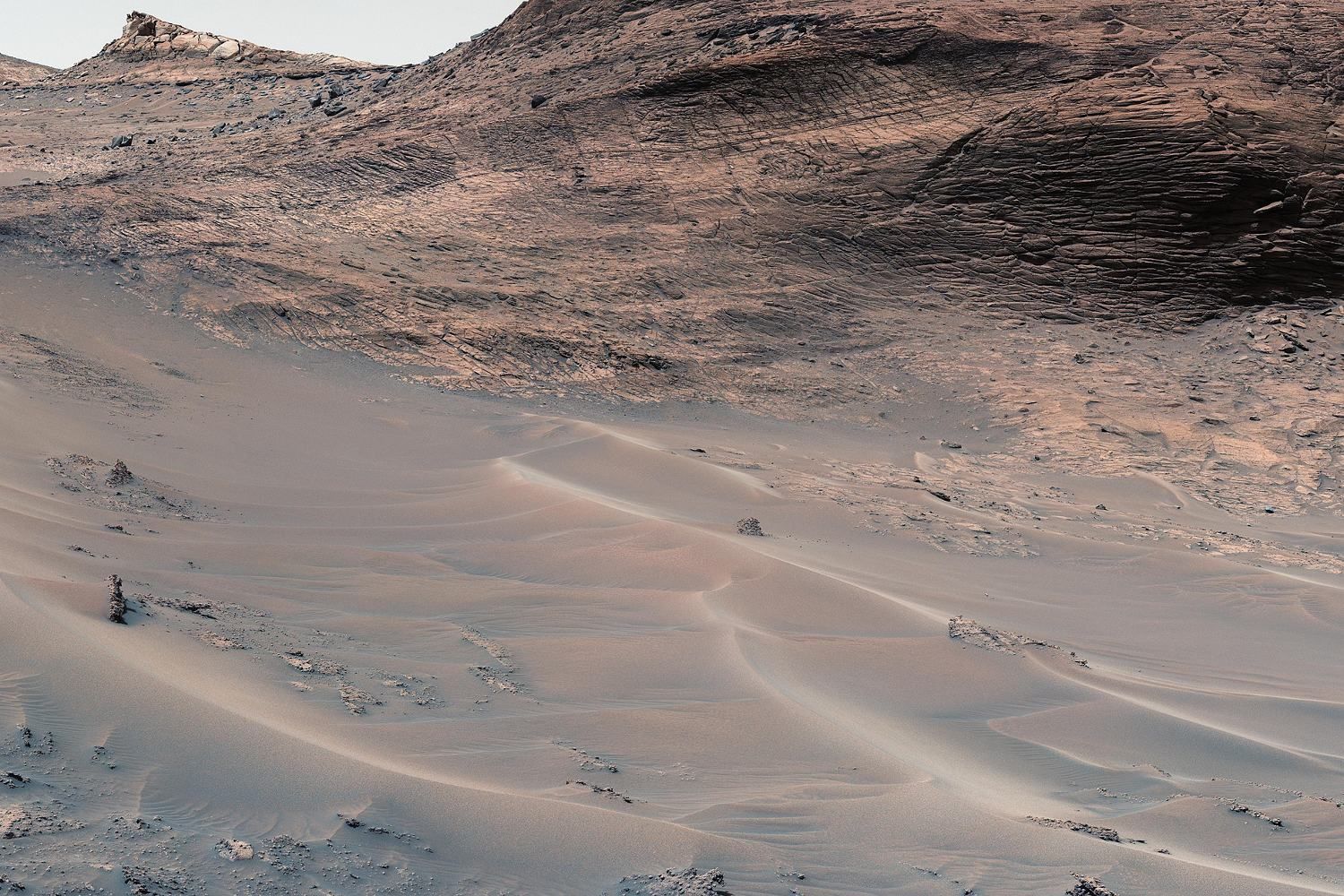 Pale wind-carved sand ridges at the foot of a dark, layered hillside.