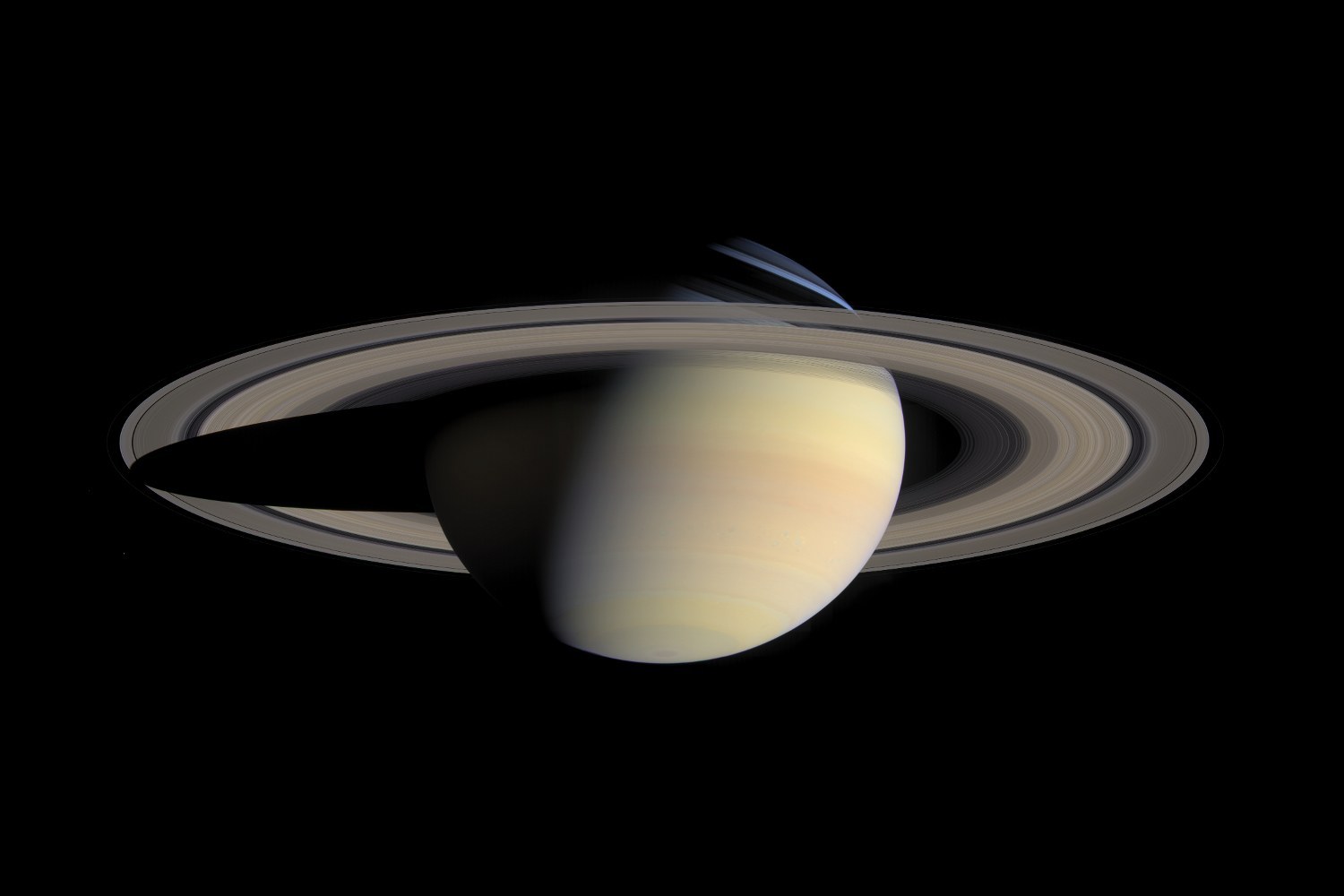 A pale, banded giant planet seen from above, its broad rings sweeping round it and its shadow falling across them.