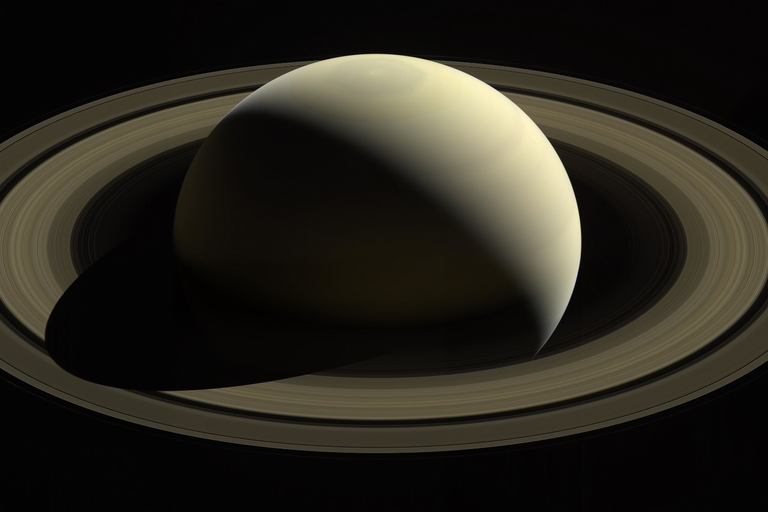 A ringed planet seen at a slant, half in shadow, its shadow cutting a dark wedge across the bright rings.