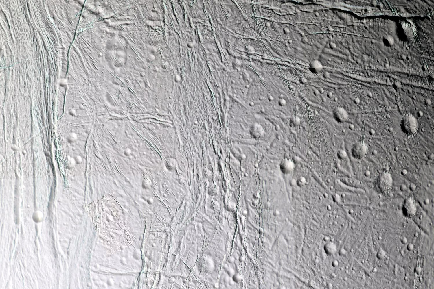 Grey-white icy ground cut by long parallel fractures and scattered craters, seen from above